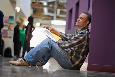 Side profile of a young man holding a textbook and sitting in a corridor Stock Photo - Premium Royalty-Free, Code: 625-02929695