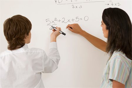 Rear view of a teenage boy solving algebra on whiteboard and a female teacher standing beside him Foto de stock - Sin royalties Premium, Código: 625-02930332