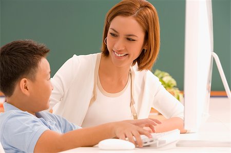 Side profile of a schoolboy with his teacher in front of a computer and smiling Stock Photo - Premium Royalty-Free, Code: 625-02930447