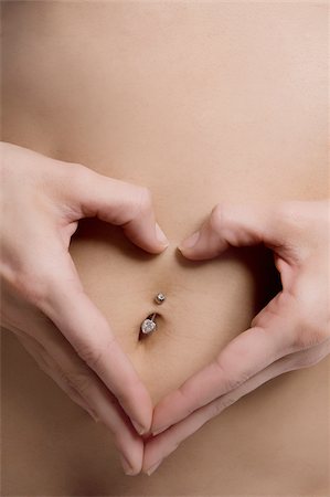 Close-up of a young woman forming heart shape with her fingers on her belly button Stock Photo - Premium Royalty-Free, Code: 625-02930699