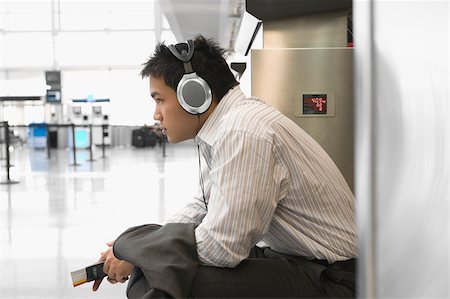 Side profile of a businessman wearing listening to headphones at an airport Stock Photo - Premium Royalty-Free, Code: 625-02932644