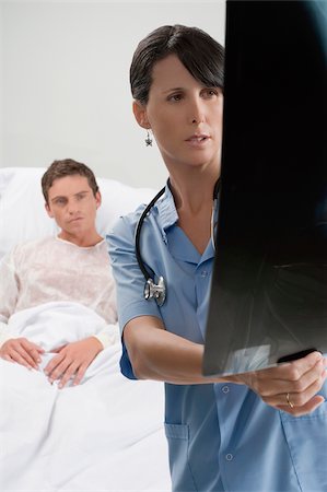 radiology patient - Female surgeon examining an X-Ray report with a patient in the background Stock Photo - Premium Royalty-Free, Code: 625-02932694