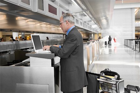 Side profile of a businessman using a laptop at an airport check-in counter Stock Photo - Premium Royalty-Free, Code: 625-02932818