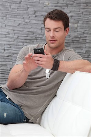 simsearch:628-07072884,k - Brunette man in T-shirt using cell phone on couch Stock Photo - Premium Royalty-Free, Code: 628-07072900