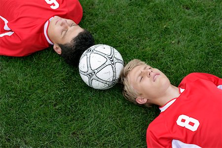 Soccer player lying head to head on grass, football between them Stock Photo - Premium Royalty-Free, Code: 628-00920073