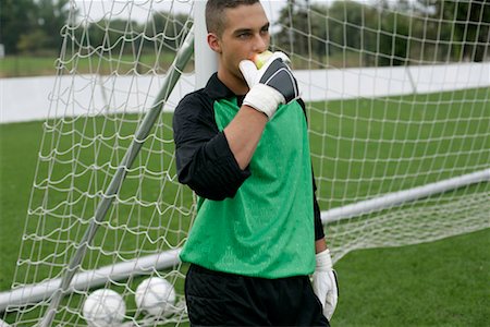 Goalkeeper eating an apple, leaning against a goal post Stock Photo - Premium Royalty-Free, Code: 628-00920099