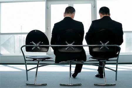Two businessmen sitting on a bench looking down, rear view Stock Photo - Premium Royalty-Free, Code: 628-00920499