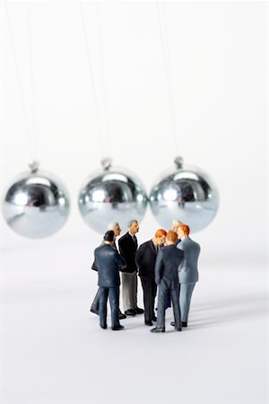 symbol for intelligence - Group of businessmen figurines standing in circle, Newton's cradle in background Stock Photo - Premium Royalty-Free, Code: 628-01278509