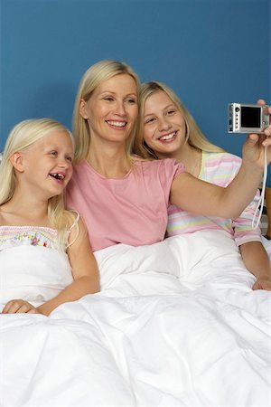 Mother sitting in bed between her two blond daughters while taking a picture of herself and her children, close-up Stock Photo - Premium Royalty-Free, Code: 628-01278656