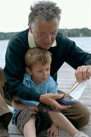 Gray-haired man with a boy in front of him is repairing a boat, selective focus Stock Photo - Premium Royalty-Free, Code: 628-01279434