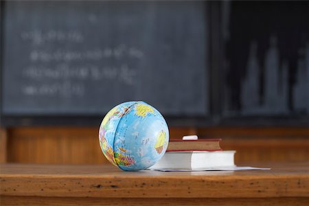 Miniature globe and book on a desk in front of a blackboard, selective focus Stock Photo - Premium Royalty-Free, Code: 628-01279603