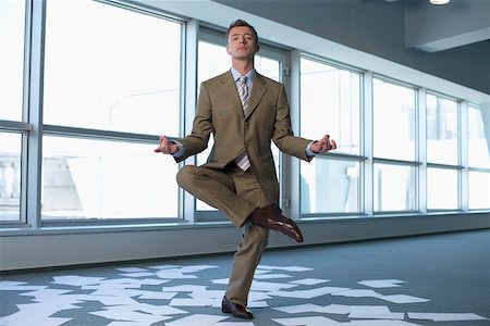 Meditating businessman in an empty office, sheets of paper on floor Stock Photo - Premium Royalty-Free, Code: 628-01639114