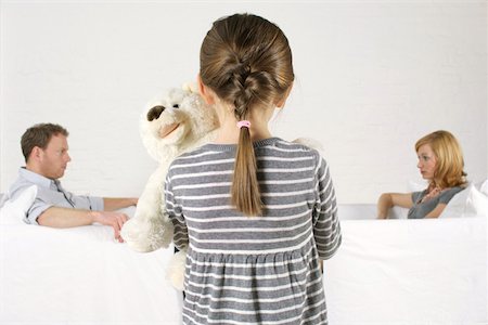 Frustrated couple sitting vis-à- vis, girl holding teddy bear standing in foreground Stock Photo - Premium Royalty-Free, Code: 628-02197912