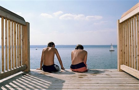 Two Boys sitting next to each other on the Edge of a Footbridge - Swimming - Friendship - Leisure Time - Youth - Lake Stock Photo - Premium Royalty-Free, Code: 628-02615702