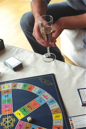 entertainment and game - Man holding a Champagne Glass and a Board Game laying on a Table (cropped) Stock Photo - Premium Royalty-Free, Code: 628-03201315