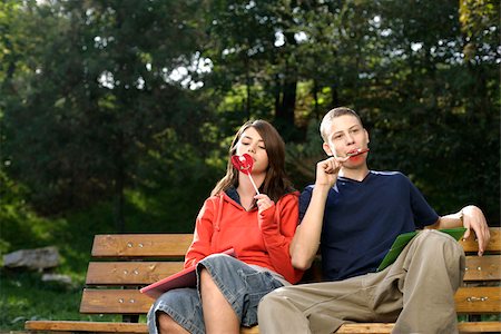 Teenage couple sitting on a bench and licking a lollypop Stock Photo - Premium Royalty-Free, Code: 628-03201385