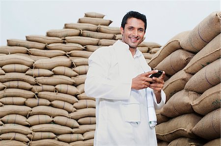 farm phone - Man standing near stacks of wheat sack holding a mobile phone, Anaj Mandi, Sohna, Gurgaon, Haryana, India Foto de stock - Sin royalties Premium, Código: 630-07071181