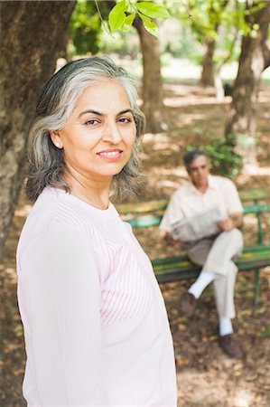 Woman leaning against a tree with her husband reading a newspaper in the background, Lodi Gardens, New Delhi, India Stock Photo - Premium Royalty-Free, Code: 630-07071296