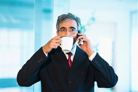 Businessman talking on a mobile phone and drinking coffee Stock Photo - Premium Royalty-Free, Code: 630-07071456