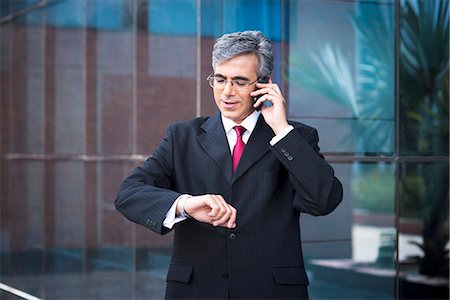 Businessman talking on a mobile phone and looking at his wristwatch Photographie de stock - Premium Libres de Droits, Code: 630-07071467
