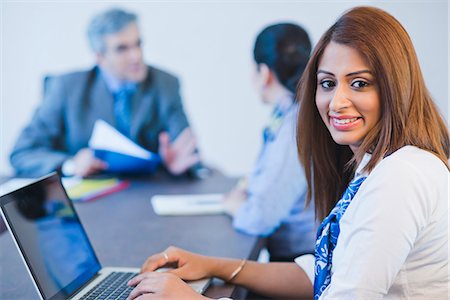 simsearch:630-07071502,k - Portrait of a businesswoman working on a laptop with her colleagues discussing in the background Stock Photo - Premium Royalty-Free, Code: 630-07071471