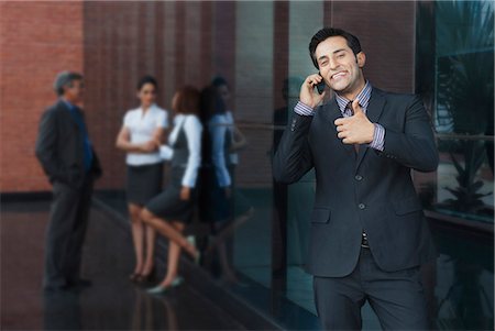 simsearch:630-07071502,k - Businessman talking on a mobile phone with their colleagues in the background Stock Photo - Premium Royalty-Free, Code: 630-07071592