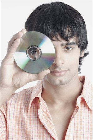 Portrait of a young man holding a compact disk in front of his face Stock Photo - Premium Royalty-Free, Code: 630-01078009
