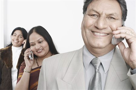 Gros plan d'un homme d'affaires parlant sur un téléphone portable avec deux femmes matures, debout derrière lui Photographie de stock - Premium Libres de Droits, Code: 630-01079386