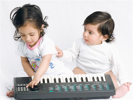 Close-up of a baby girl playing an electronic piano with her brother sitting beside her Stock Photo - Premium Royalty-Free, Code: 630-01079579