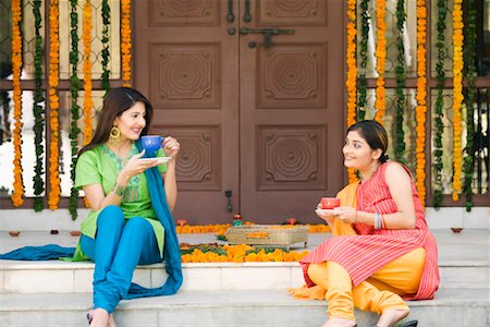 Two young women sitting at doorstep of a house and holding cups of tea Stock Photo - Premium Royalty-Free, Code: 630-01192189