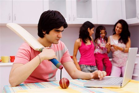 Young man holding a cricket bat and using a laptop in the kitchen Stock Photo - Premium Royalty-Free, Code: 630-01192843