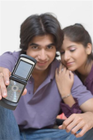 Portrait of a young man showing "I Love You" on his mobile phone with a young woman leaning on him Stock Photo - Premium Royalty-Free, Code: 630-01490857