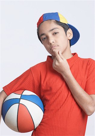 Portrait of a boy holding a basketball with his finger on his chin Stock Photo - Premium Royalty-Free, Code: 630-01491548