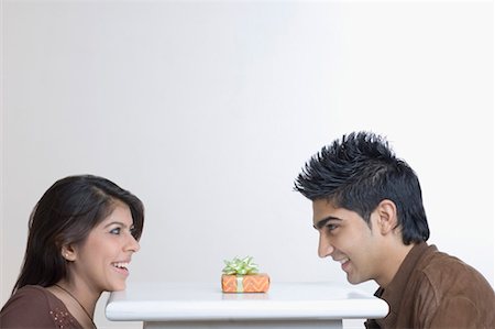 Side profile of a young couple sitting at a table with a present on it Stock Photo - Premium Royalty-Free, Code: 630-01491590