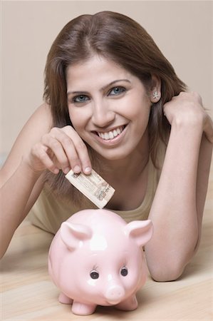 Portrait of a young woman putting money in a piggy bank Stock Photo - Premium Royalty-Free, Code: 630-01491614