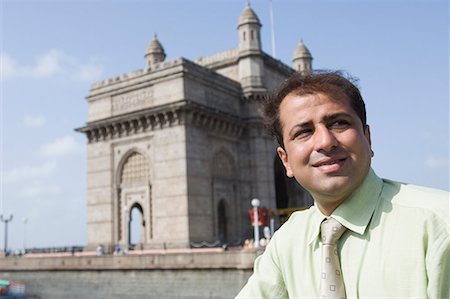 Close-up of a businessman smiling with monument in the background, Gateway of India, Mumbai, Maharashtra, India Stock Photo - Premium Royalty-Free, Code: 630-01708702