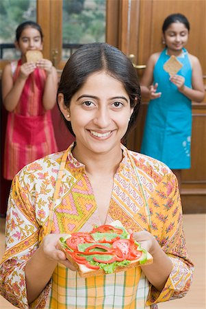 pic of indian kid eating breakfast - Close-up of a mid adult woman holding a sandwich with her daughters in the background Stock Photo - Premium Royalty-Free, Code: 630-01709138