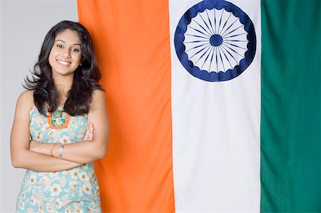 Portrait of a young woman standing with her arms crossed in front of an Indian flag Stock Photo - Premium Royalty-Free, Code: 630-01709910