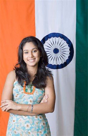 Portrait of a young woman standing with her arms crossed in front of an Indian flag Stock Photo - Premium Royalty-Free, Code: 630-01709911