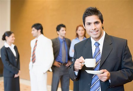 Portrait of a businessman holding a cup of tea with his colleagues standing behind him Stock Photo - Premium Royalty-Free, Code: 630-01874024