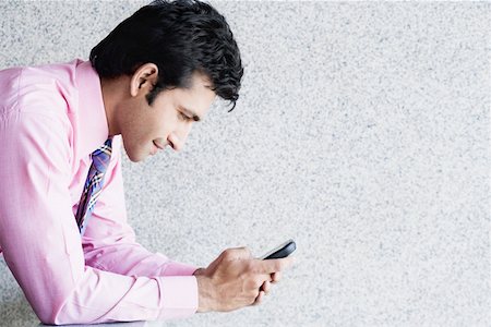 Side profile of a businessman text messaging on a mobile phone Stock Photo - Premium Royalty-Free, Code: 630-01874421