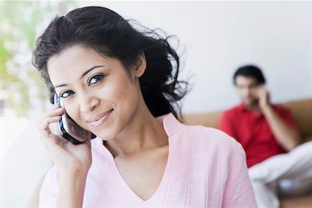 Portrait of a young woman talking on a mobile phone with a young man sitting in the background Stock Photo - Premium Royalty-Free, Code: 630-01874572