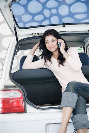 Young woman sitting in a car trunk and talking on a mobile phone Stock Photo - Premium Royalty-Free, Code: 630-01874781