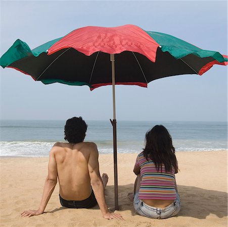 Rear view of a young couple sitting under a beach umbrella on the beach Stock Photo - Premium Royalty-Free, Code: 630-01877067