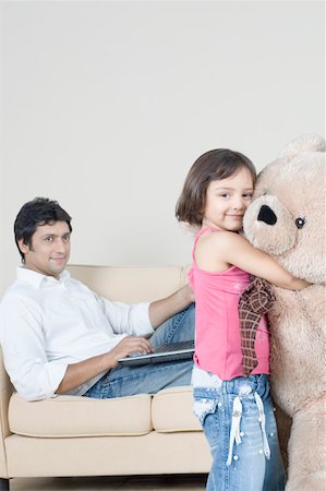 shirt rolled sleeves - Portrait of a girl hugging a teddy bear with her father using a laptop beside her Stock Photo - Premium Royalty-Free, Code: 630-01877165