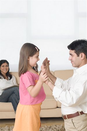 patty cake photos - Side profile of a girl playing with her father and her mother sitting on a couch in the background Stock Photo - Premium Royalty-Free, Code: 630-01877511