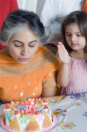 Close-up of a mature woman blowing candles on a birthday cake with her granddaughter standing beside her Stock Photo - Premium Royalty-Free, Code: 630-01877572