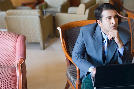 Homme assis devant un ordinateur portable avec sa main sur son menton Photographie de stock - Premium Libres de Droits, Code: 630-01873127