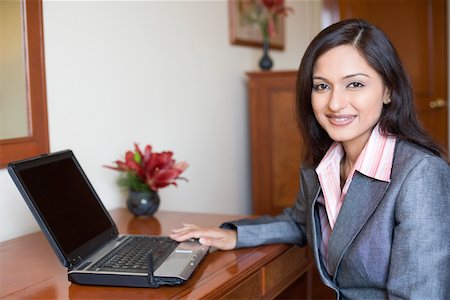 Portrait d'une femme d'affaires assis devant un ordinateur portable et souriant Photographie de stock - Premium Libres de Droits, Code: 630-01873301