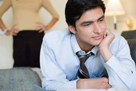 Close-up of a businessman lying on the bed with a young woman standing in the background Stock Photo - Premium Royalty-Free, Code: 630-01873313